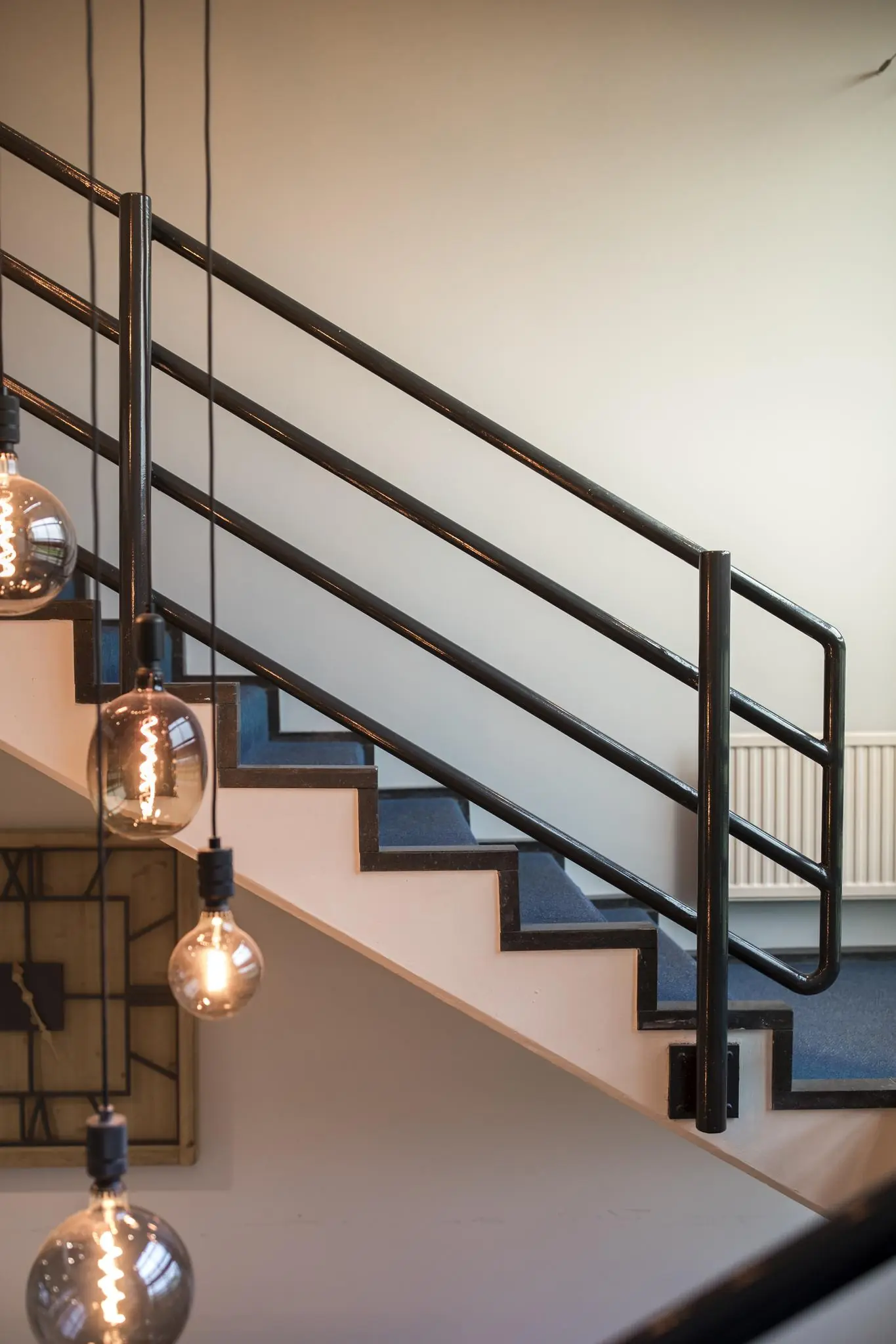 Moderne trap met blauwe bekleding, zwarte leuning en hangende gloeilampen in een interieur aan de Markerkant 13.